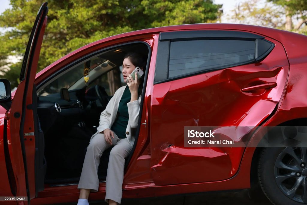 Driver on the phone after a collision, sitting in her damaged car.