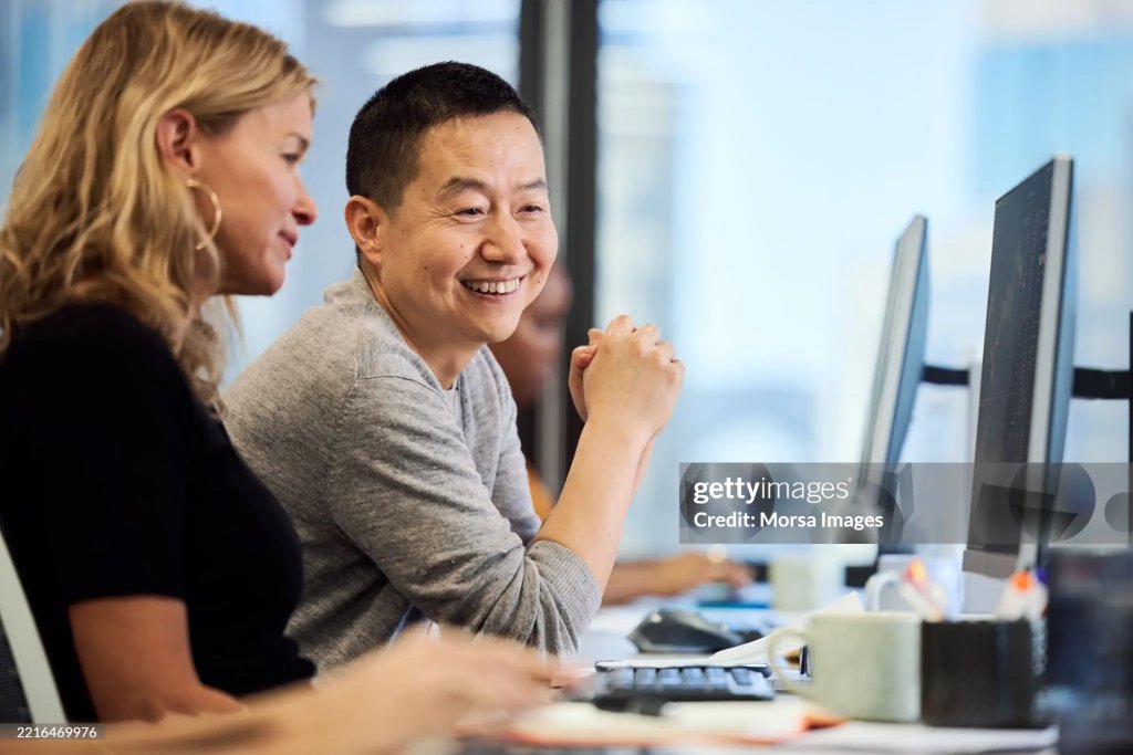 Two colleagues smiling while working at a computer in an office.