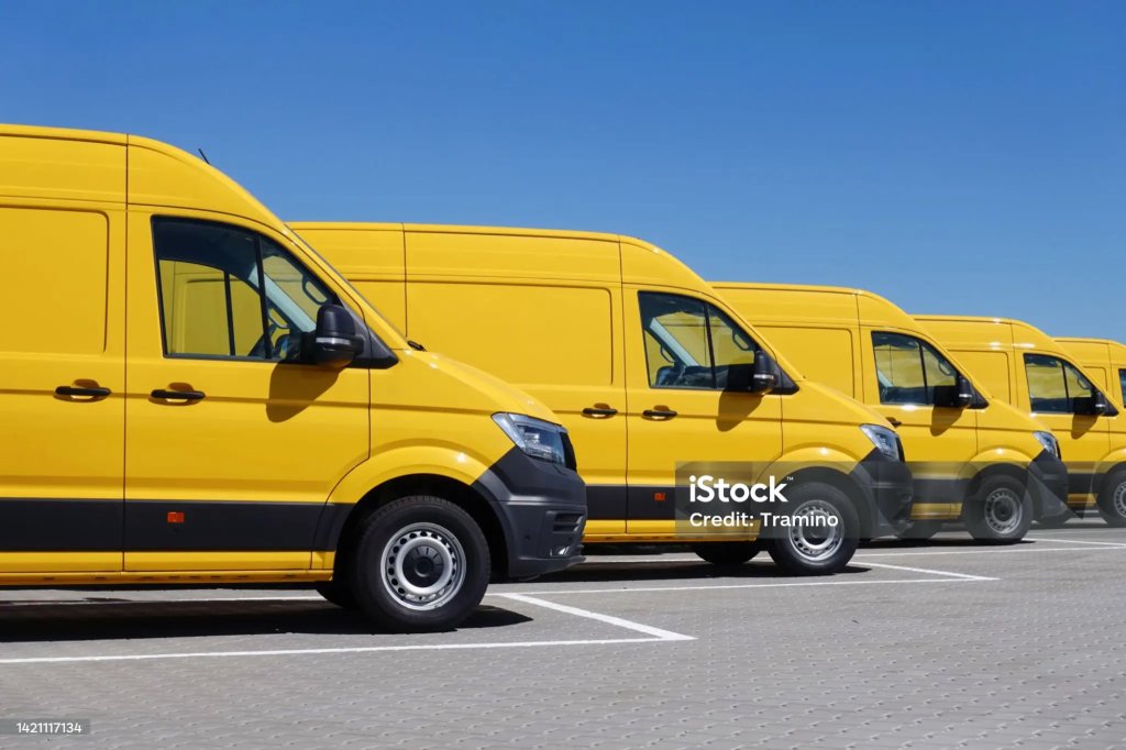 Row of yellow fleet vans parked in a depot.
