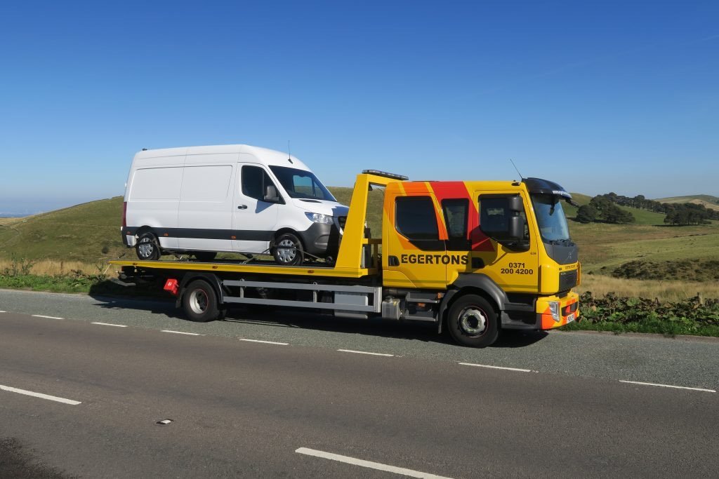 Egertons flatbed recovery truck carrying a white van along a road.