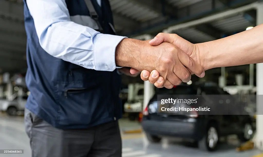 Two business partners shaking hands in a vehicle workshop.